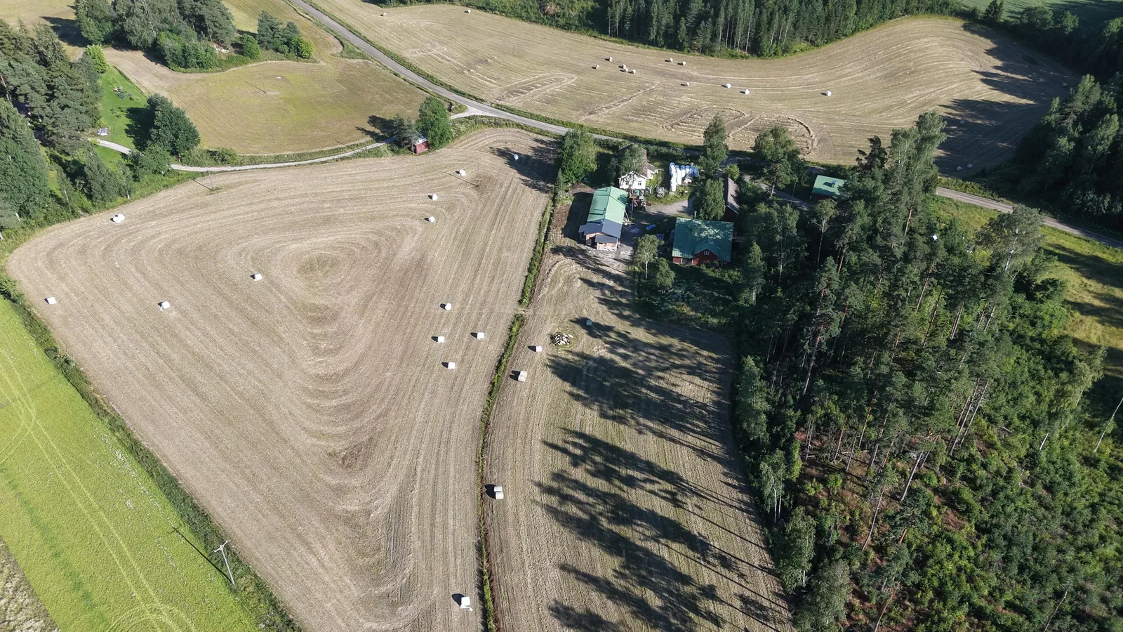 Ilmakuva Terapia Koivikon maatilasta metsän keskellä, peltoja ja tallirakennuksia